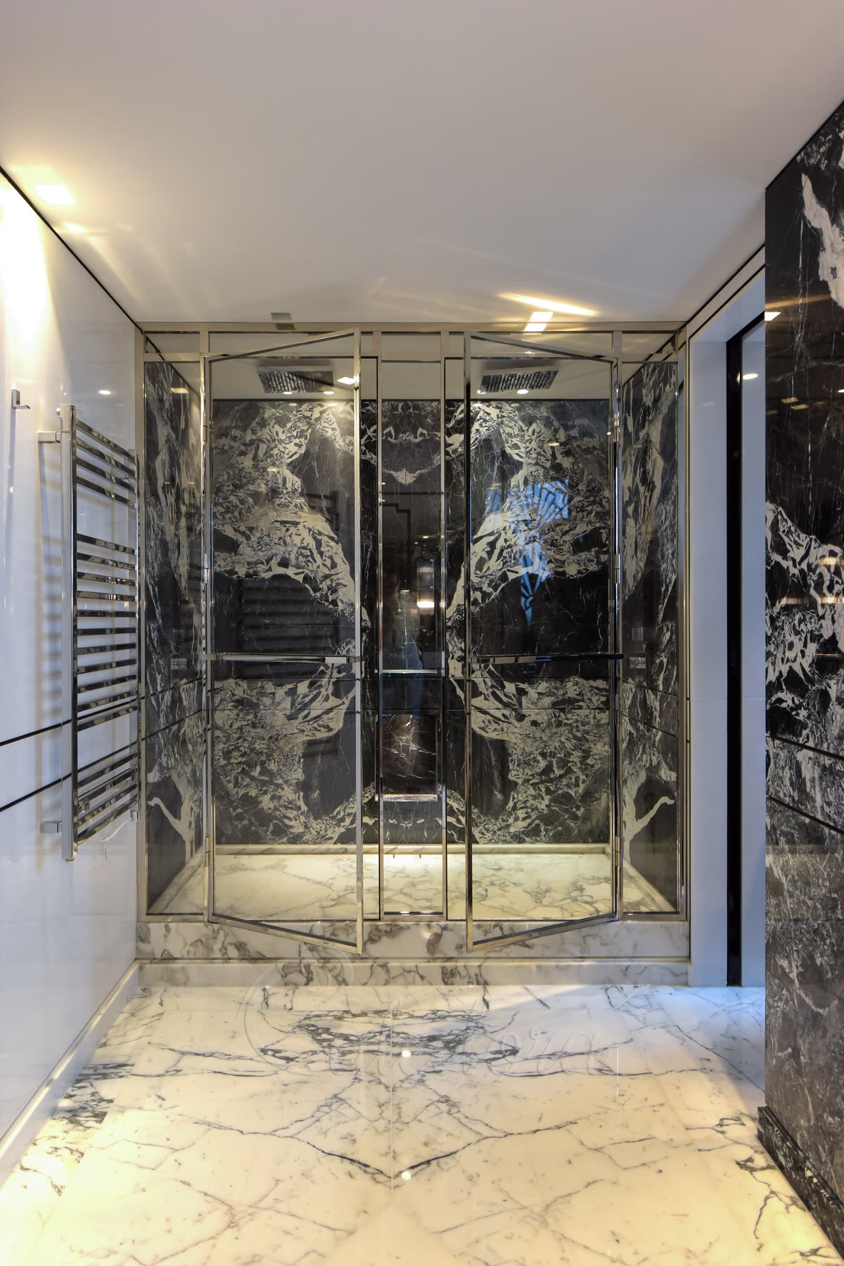 Polished nickel framed double hinged doors with 8mm ultra clear glass, twin shower heads on opposite walls for two-person use, and bespoke towel rails