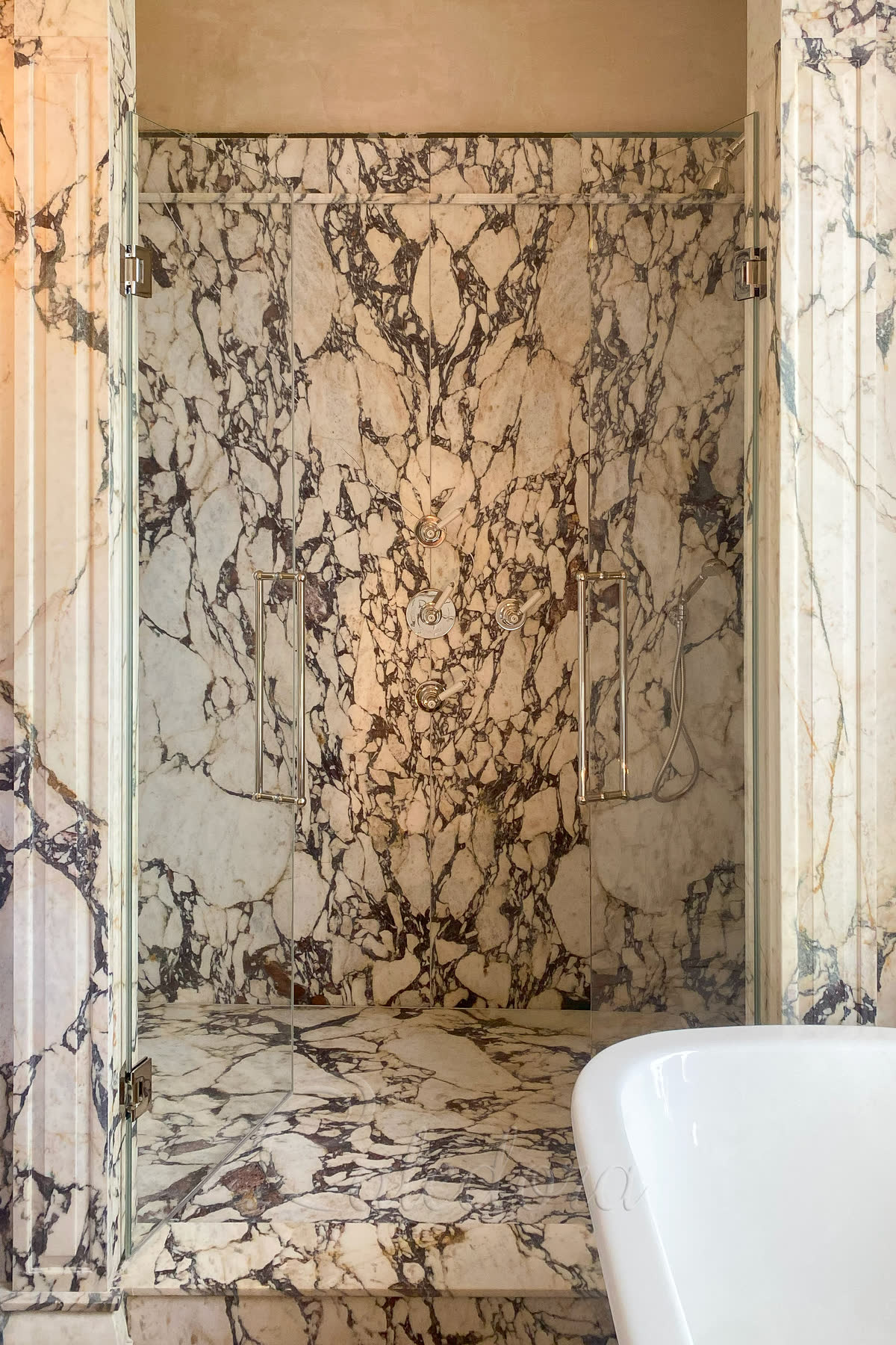 Polished nickel double hinged shower doors with 10mm ultra clear glass, flush-integrated hinges set into marble walls and long bespoke handles
