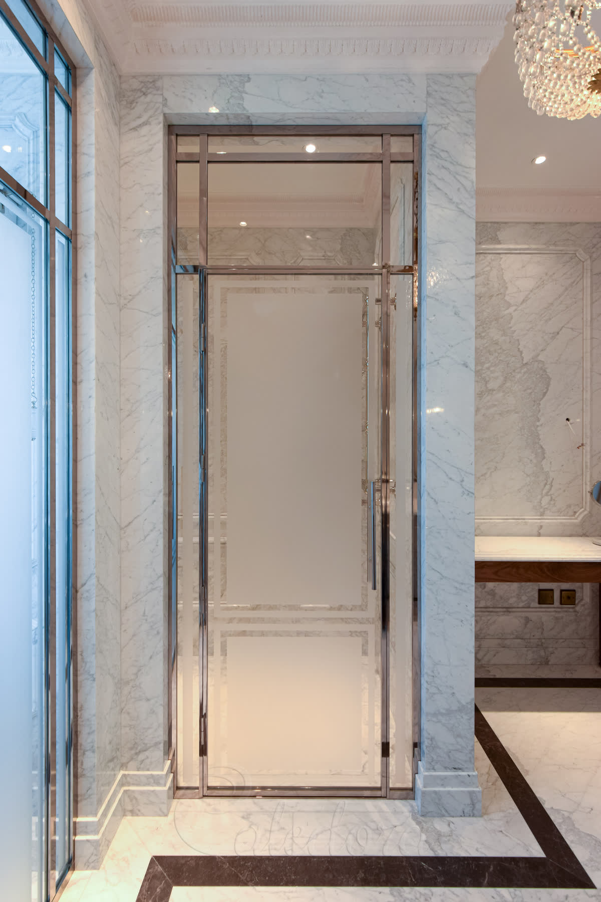 Polished nickel fully framed shower door with 8mm ultra clear glass partially sandblasted for privacy — mirror-polished frame against marble walls with a crystal chandelier above