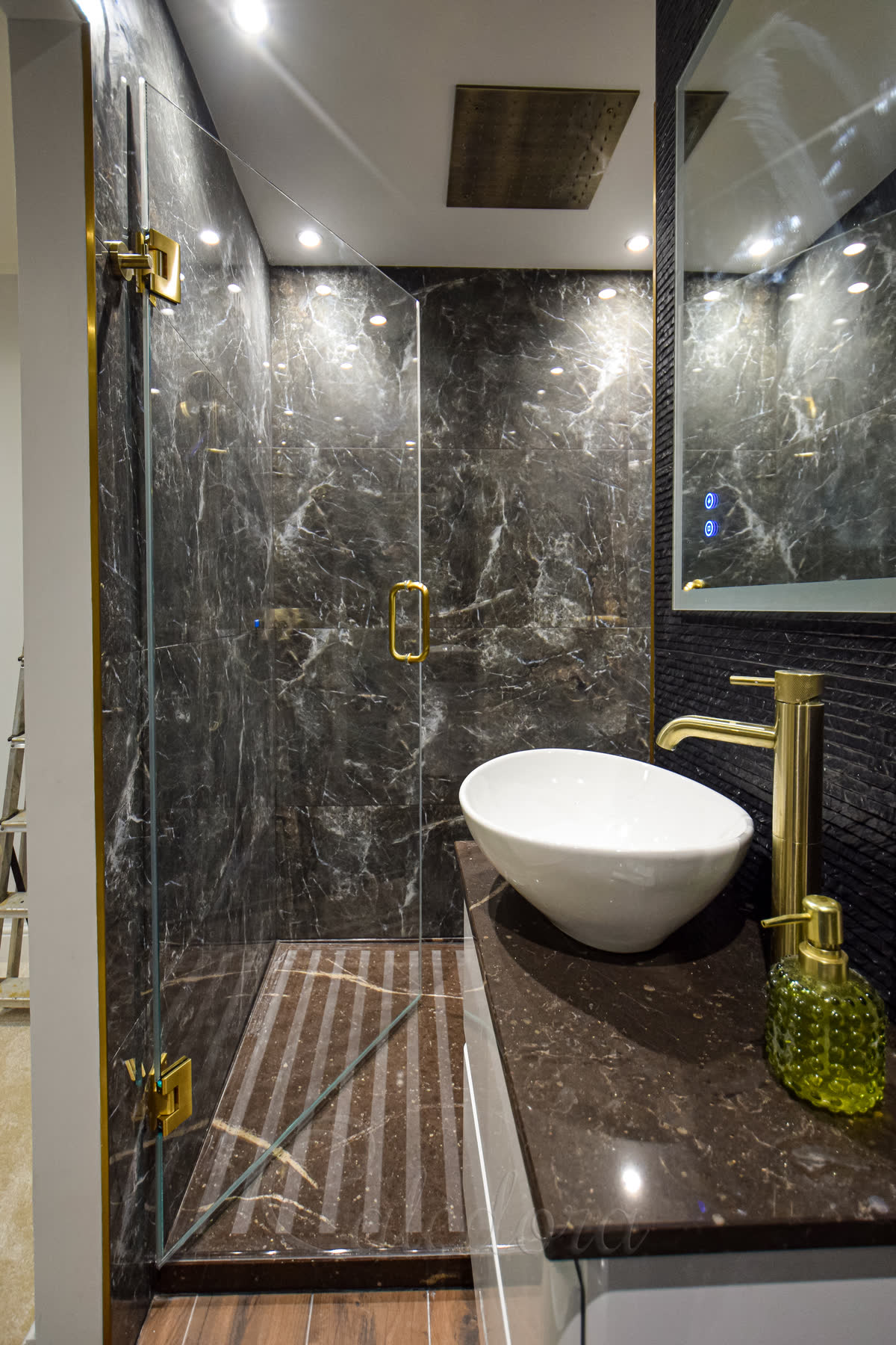 Brushed brass frameless hinged shower door (880mm wide entry) with 10mm ultra clear glass and minimalistic door seals against dark marble tile, white freestanding bath beside it