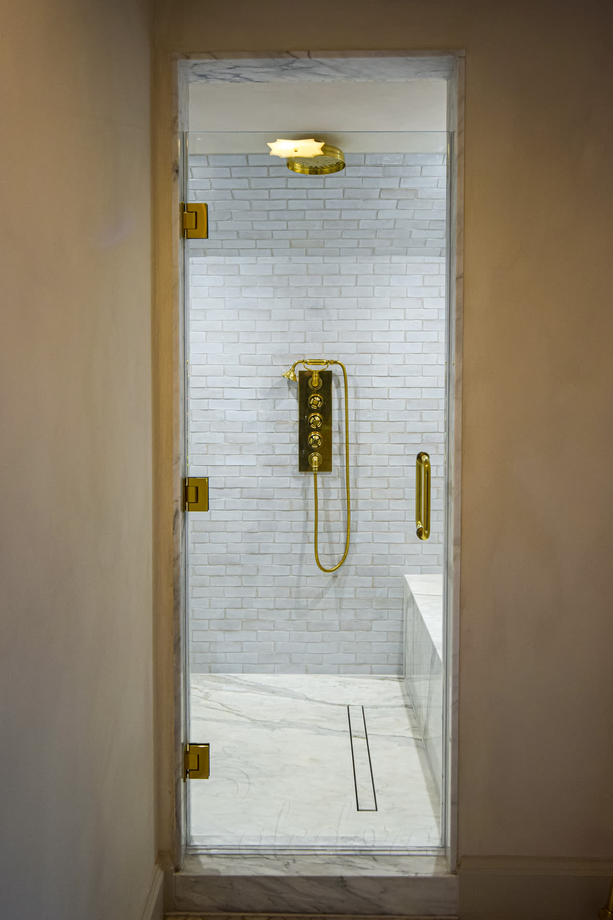 Polished gold frameless hinged shower door with three hinges and 10mm ultra clear glass, mounted against white subway tile to match the gold shower fixtures
