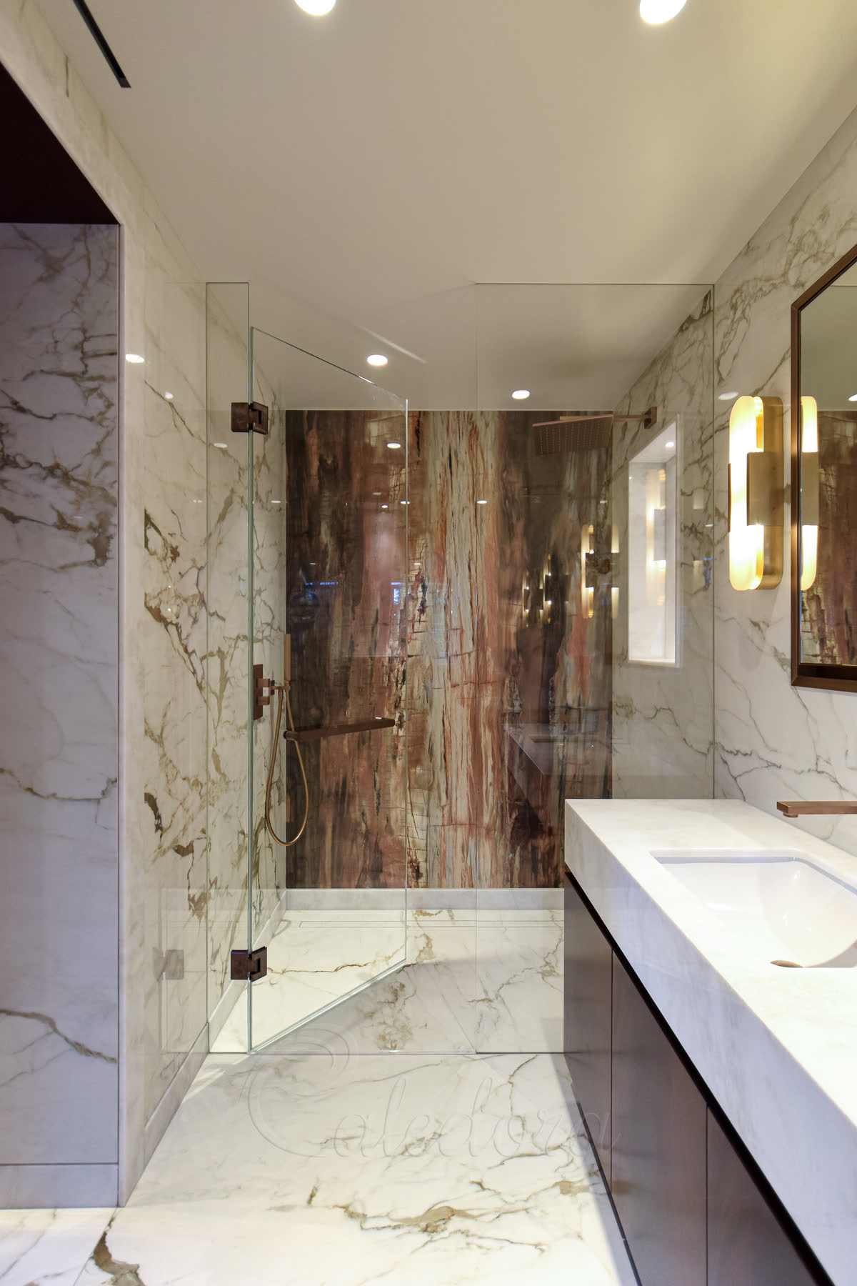 Inline copper hinged shower door swung open in a London marble bathroom — door-mounted horizontal towel rail visible on the open panel, calacatta marble walls with petrified-wood feature panel inside the enclosure