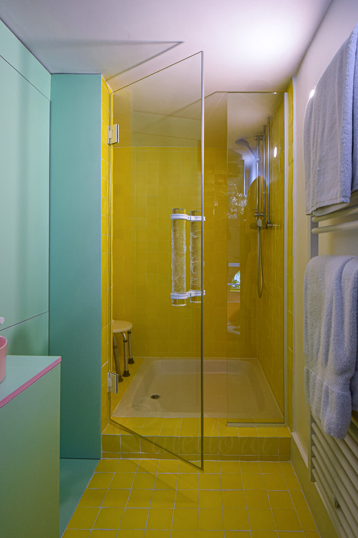 White powder-coated frameless swing shower door in open position with 10mm clear glass and a bespoke cylindrical glass handle held by white fixtures — alcove enclosure (650mm door + 350mm fixed panel)