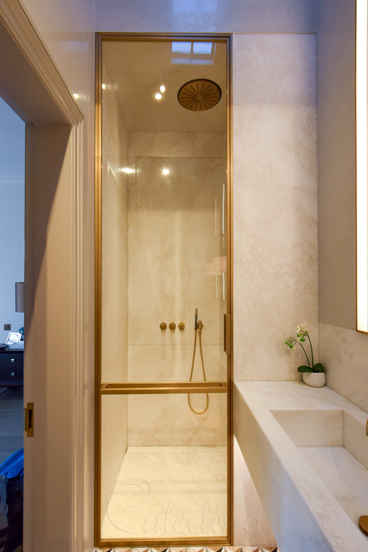 Bespoke full-height polished brass-framed shower door with round brass vent in a luxury marble bathroom