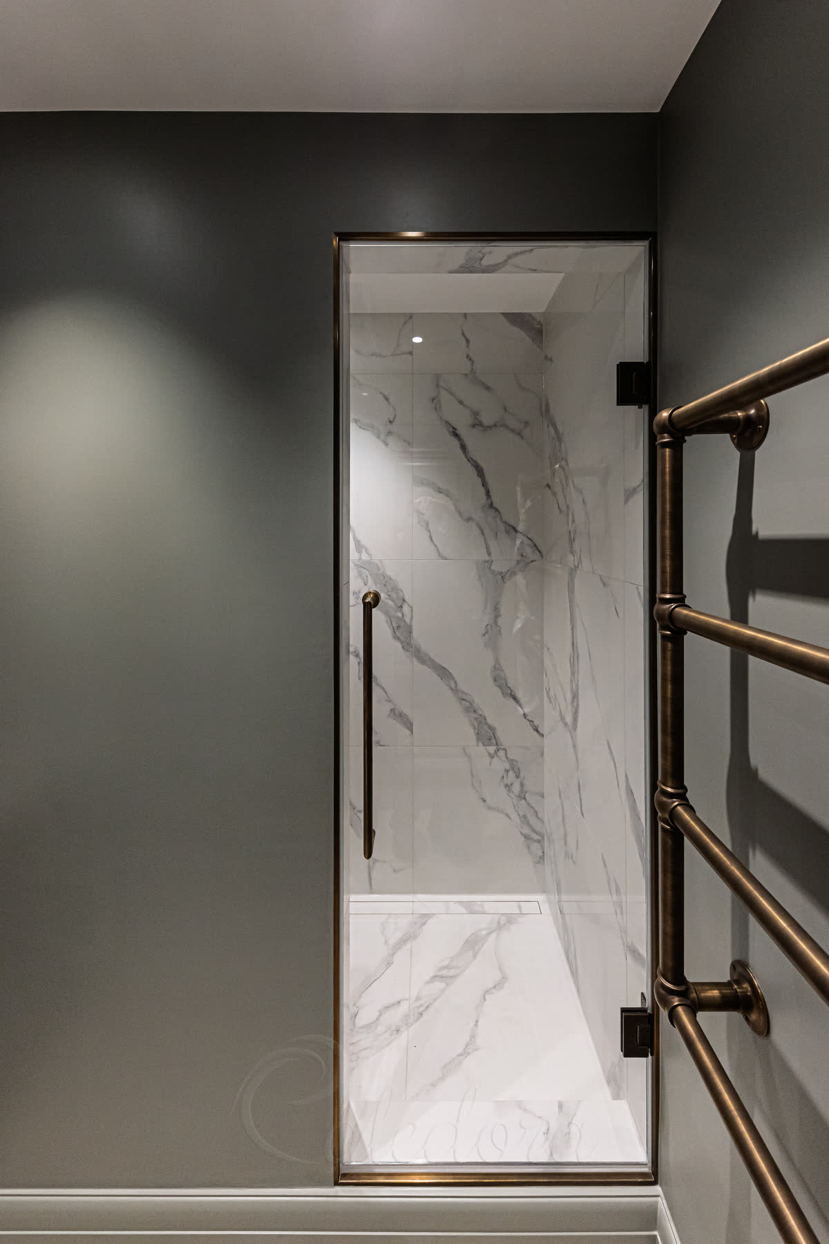 Frameless glass shower door with antique brass hinges in marble bathroom