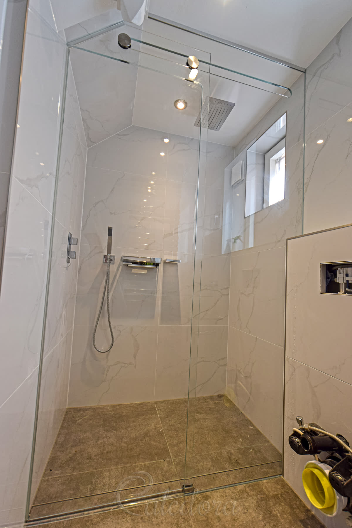 Trackless sliding glass doors with bespoke angled design following sloped ceiling line in a loft bathroom with large-format tiled walls and chrome shower fixtures