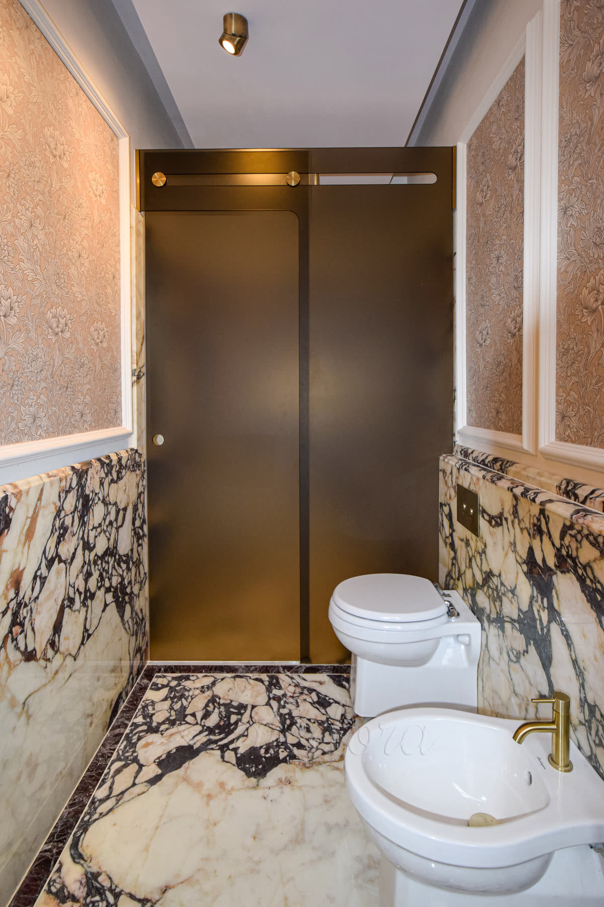 Bronze-tinted 10 mm glass with sandblasted frosted surface on a frameless trackless sliding shower in an Oxted bathroom — bronze tinting visible through the frosting, brass-coated wheels and a circular hole handle on the marble wall behind