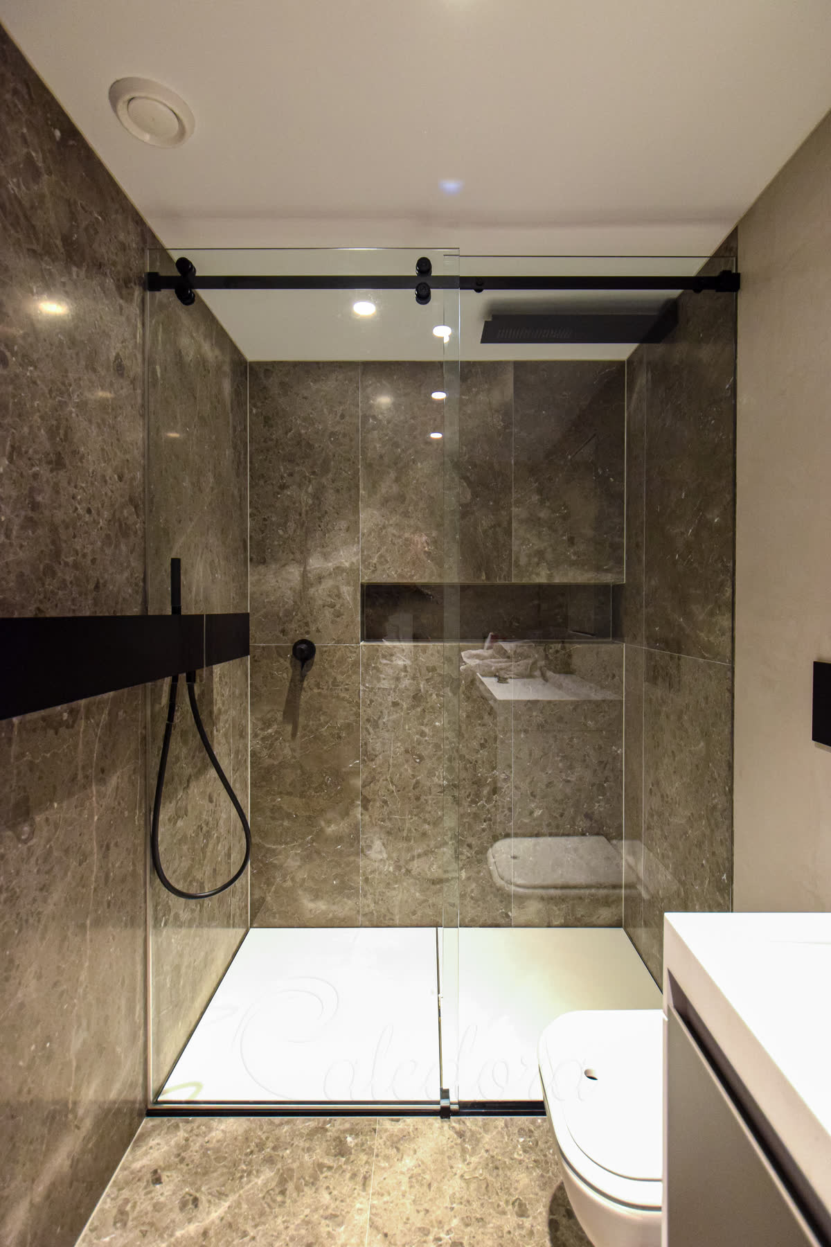 Frameless black sliding shower door with 10 mm clear glass — closed-door view showing a custom-cut notch around an existing wall-mounted shelf in a London marble bathroom