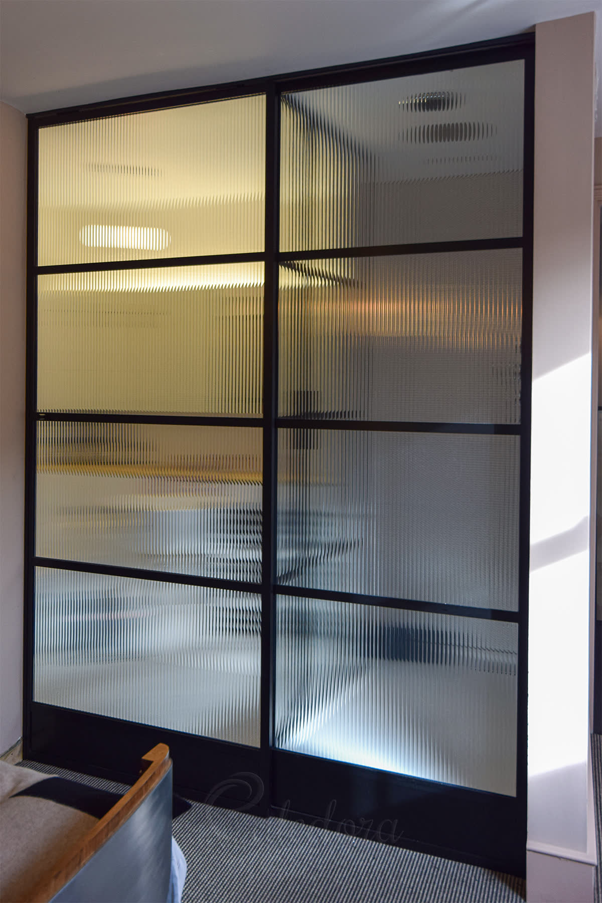 Full-height sliding shower door partition with reeded laminated glass set in a black-grid frame — framed system protects the textured surface from the floor guide and the laminated edges from water