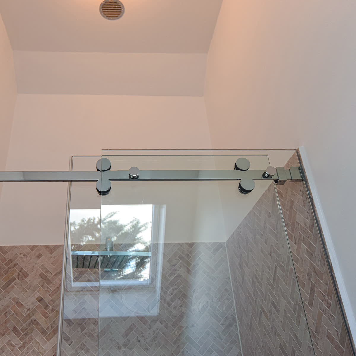 Close-up of chrome roller wheels riding a horizontal sliding-track tube above the glass — the traditional rollers-on-tube mechanism in a frameless London install