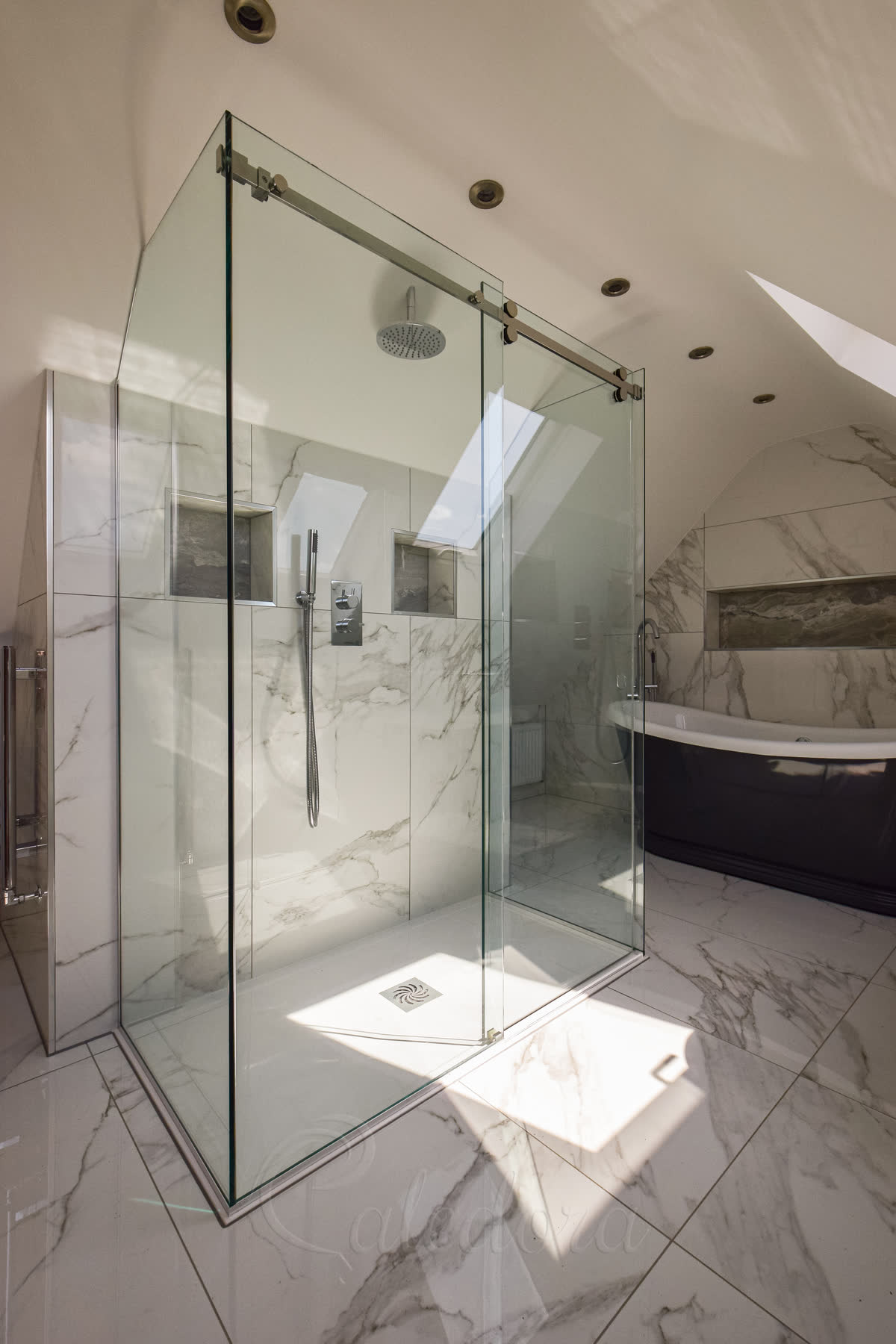 Three-sided frameless sliding shower door with chrome track in a luxury loft bathroom with marble walls, skylights and modern black bathtub