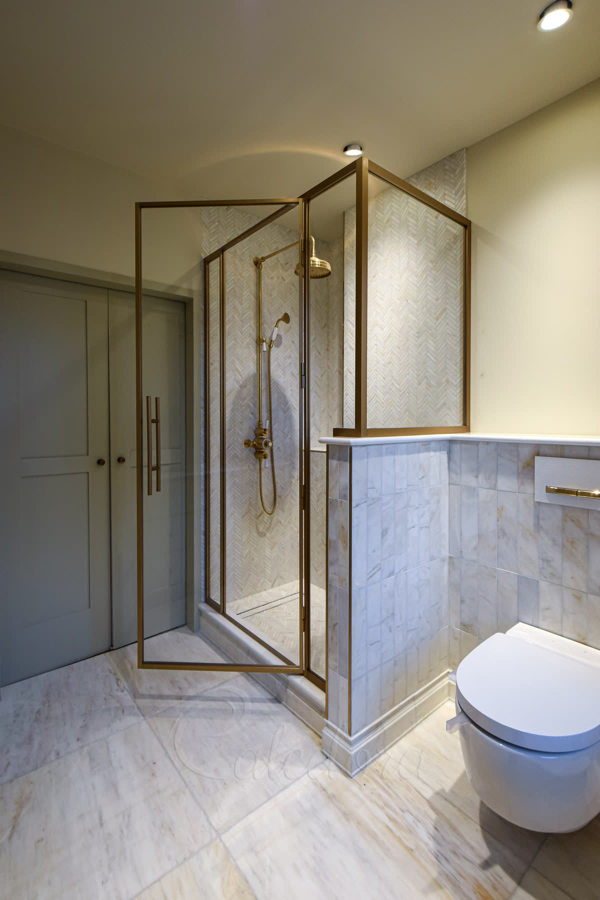 Two-sided shower enclosure with aged brass frame over tiled tray