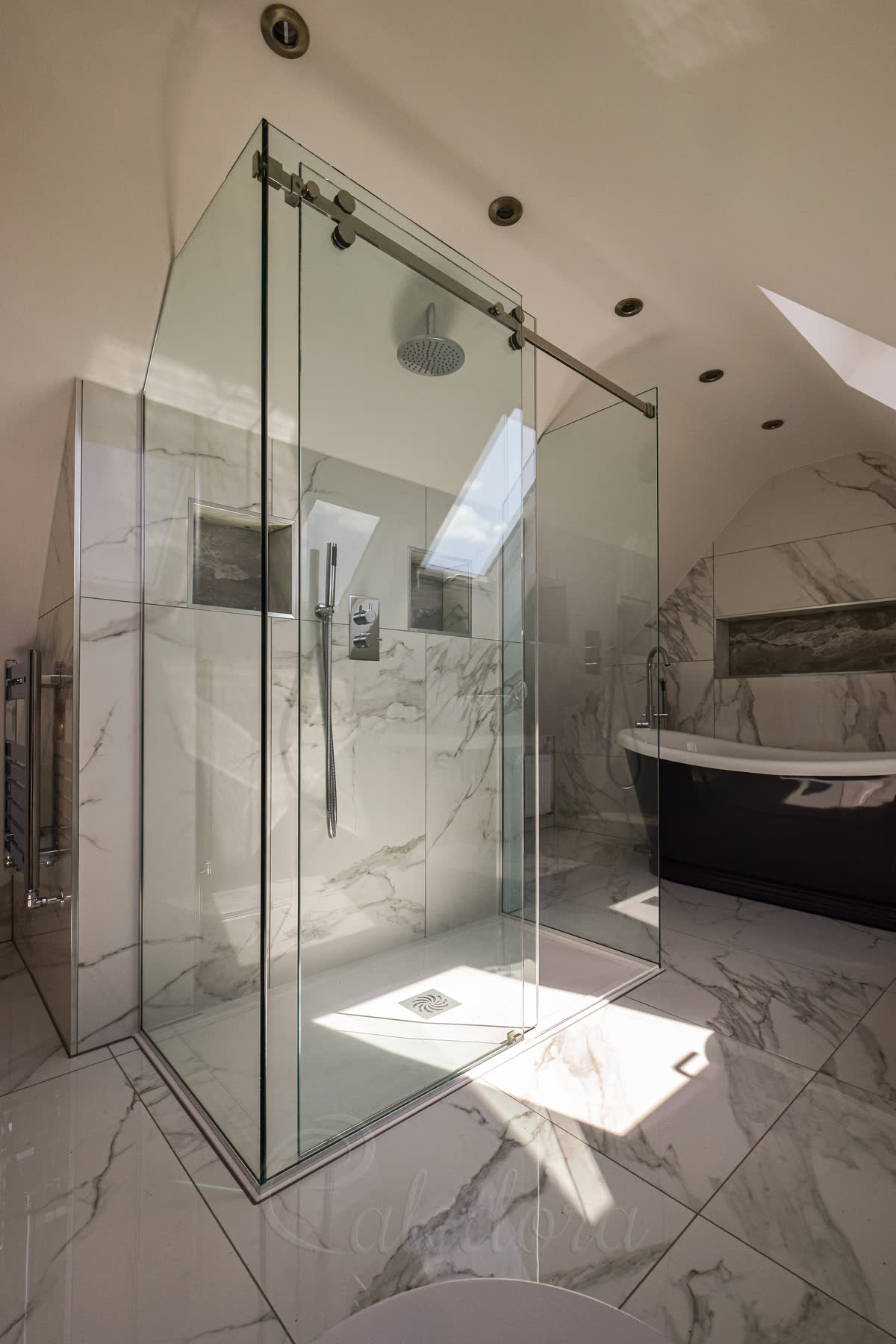 Shower enclosure over raised tray with sliding door, glass angled to sloped ceiling in marble bathroom