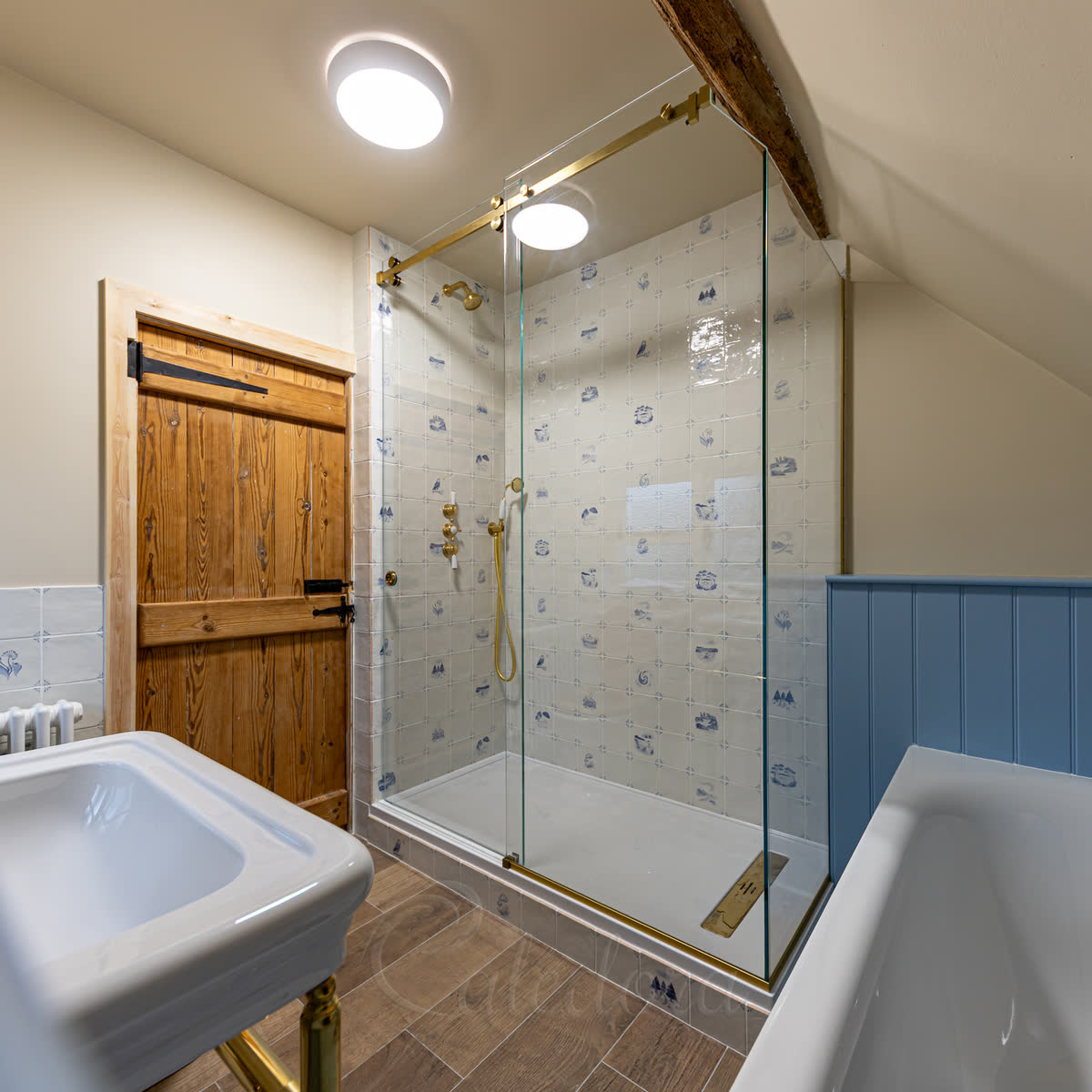 Sliding shower enclosure with brushed brass track, glass shaped to sloped loft ceiling with joist notch