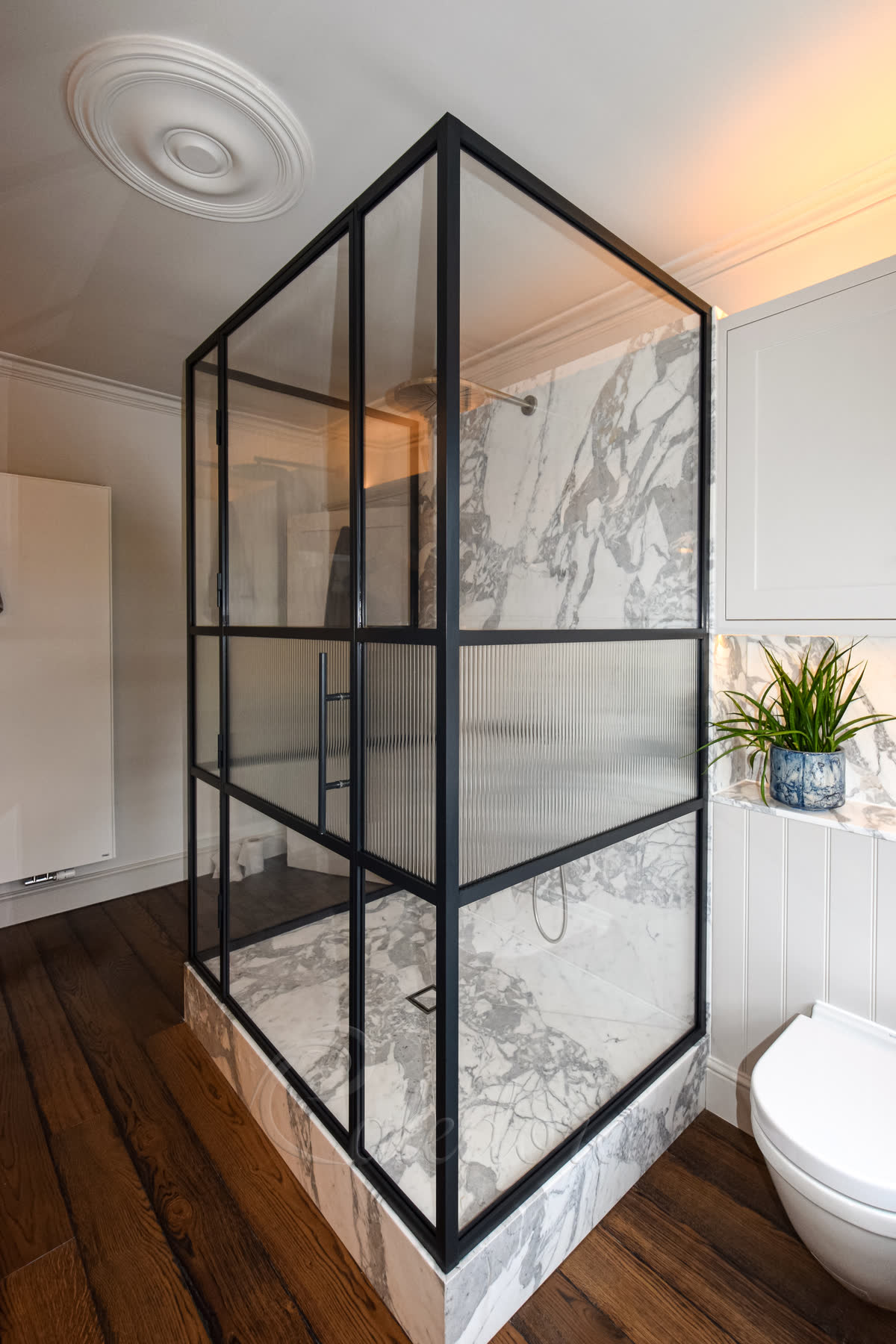 Three-sided shower enclosure with black grid frame, central fluted glass section in marble bathroom