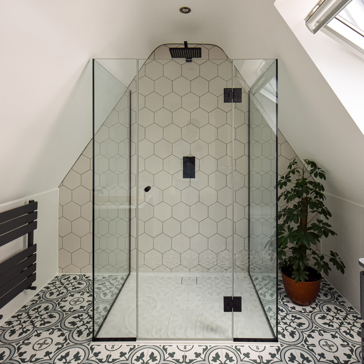 Three-sided frameless shower enclosure under loft eaves with black fixtures, reduced height design