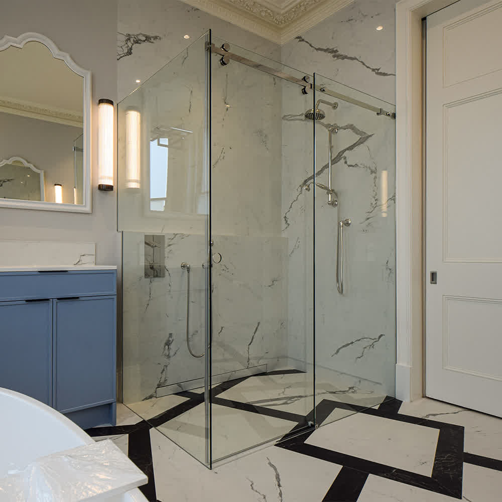 Bespoke sliding glass shower door with chrome hardware in a marble-tiled bathroom