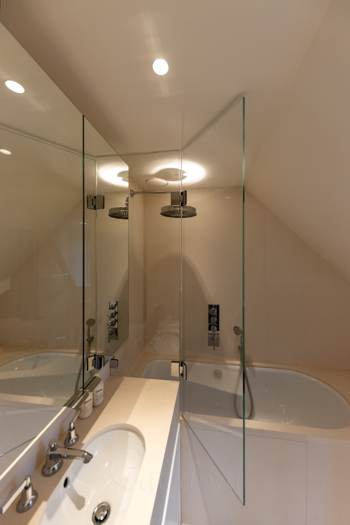 A bath screen whose fixed panel ends in line with the edge of the vanity unit, where the hinged panel starts, in a cream loft bathroom