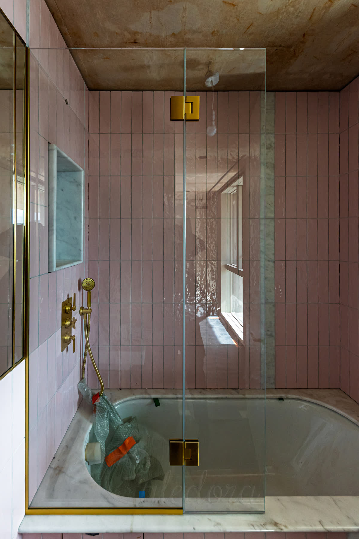 A bath screen with a flip panel on brass hinges over a marble-topped bath, with pink tiles and a brass shower