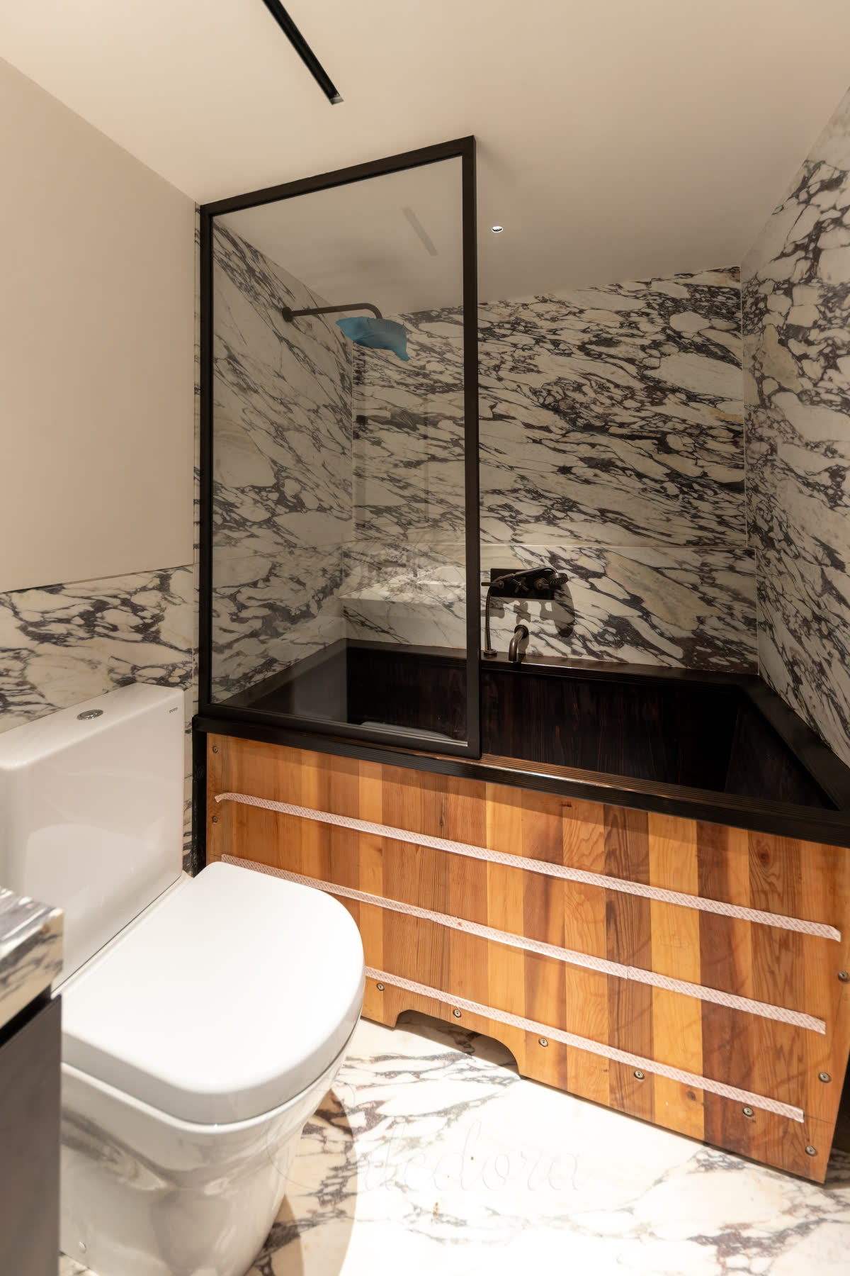 A dark bronze framed bath screen over a Japanese-style timber bath with inlaid lines, in a bathroom of purple-veined marble