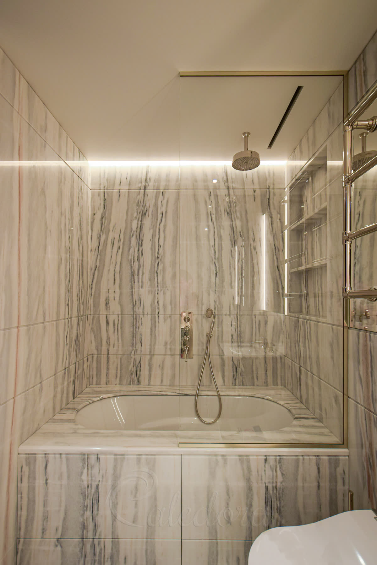 A fixed bath screen held in polished nickel channels, standing on a bath clad in veined marble
