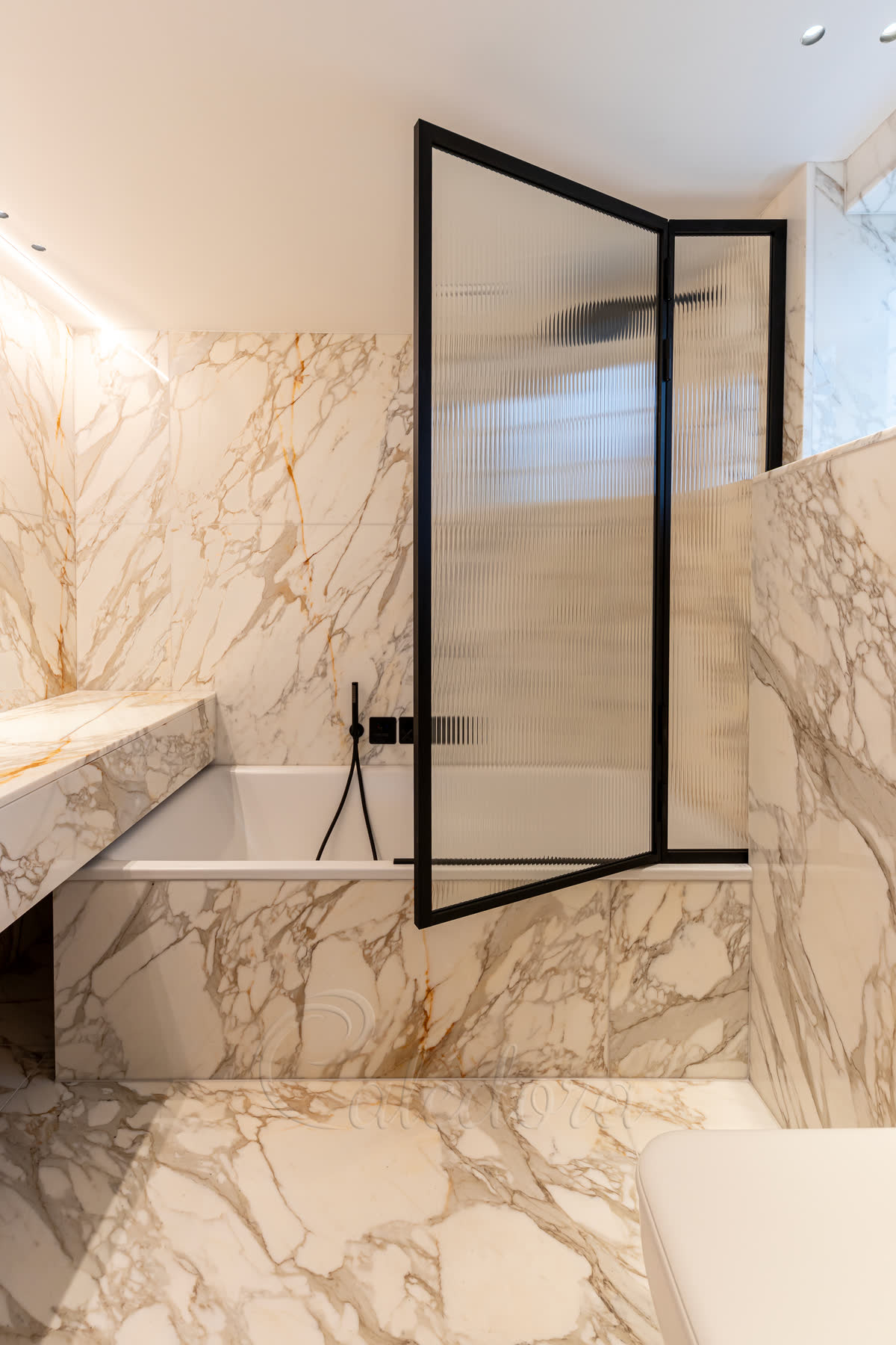 A black-framed bath screen of reeded glass swung open over a marble-panelled bath, with a marble ledge beside it