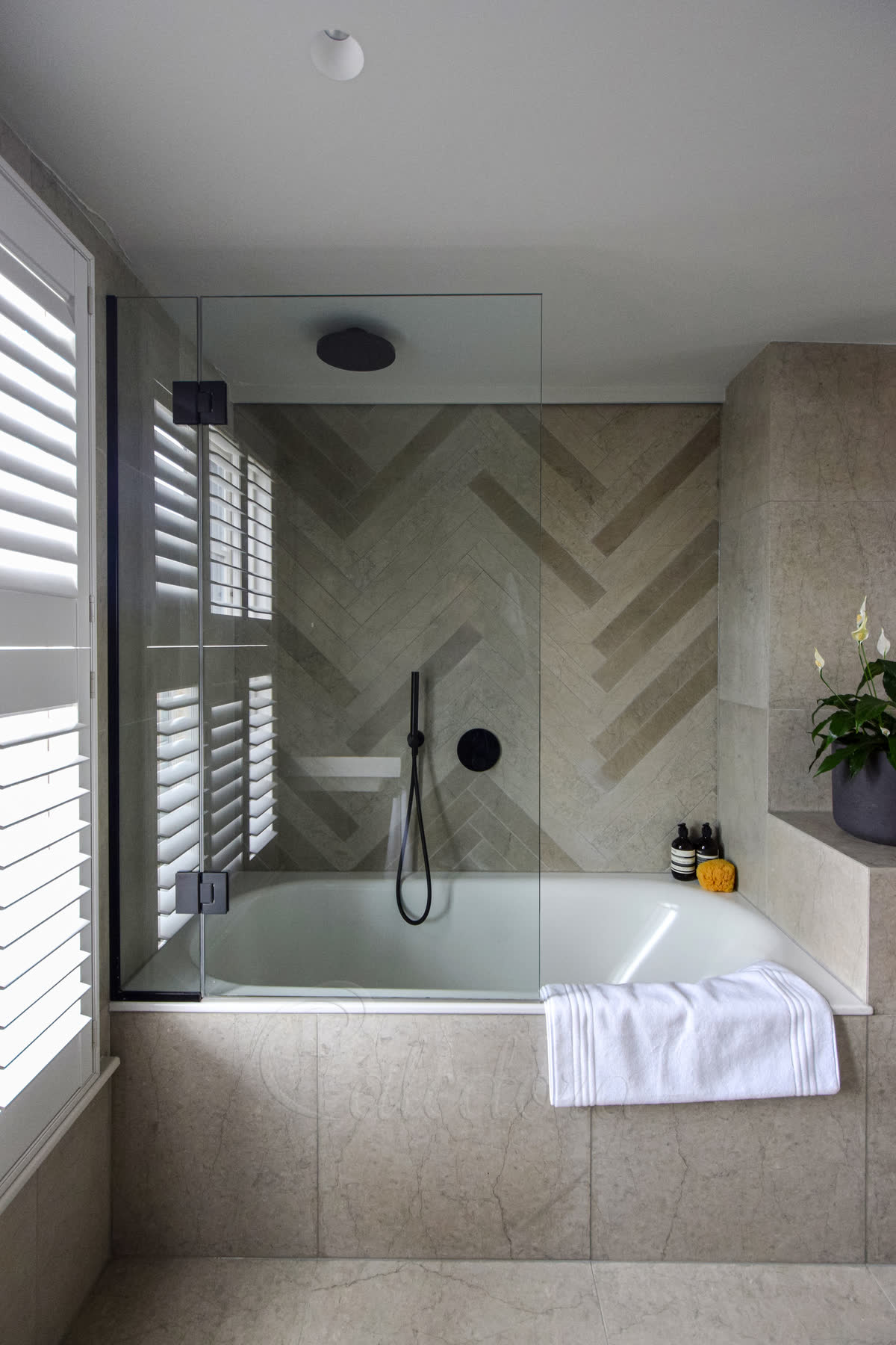 Black framed bath shower screen mounted at the end of a bath in a London bathroom