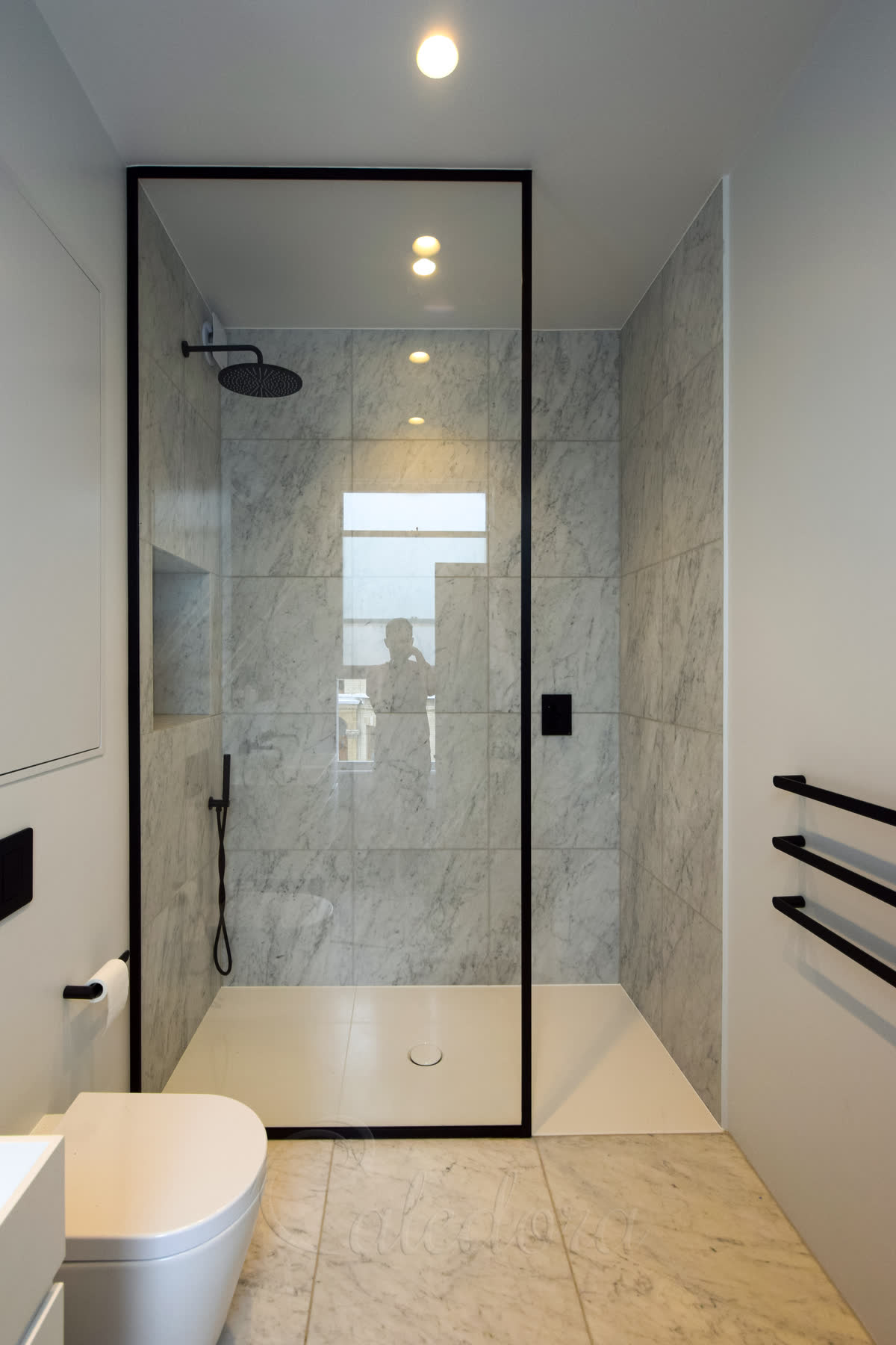 Walk-in black framed shower screen with Ultra Clear glass and marble walls in a London bathroom