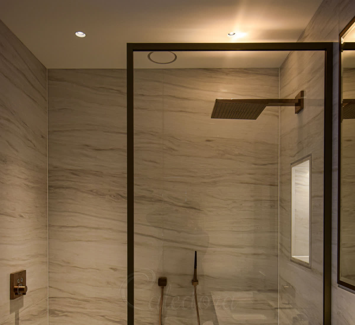 Brushed bronze shower screen aligned with bathroom mirror frame in marble-tiled London bathroom