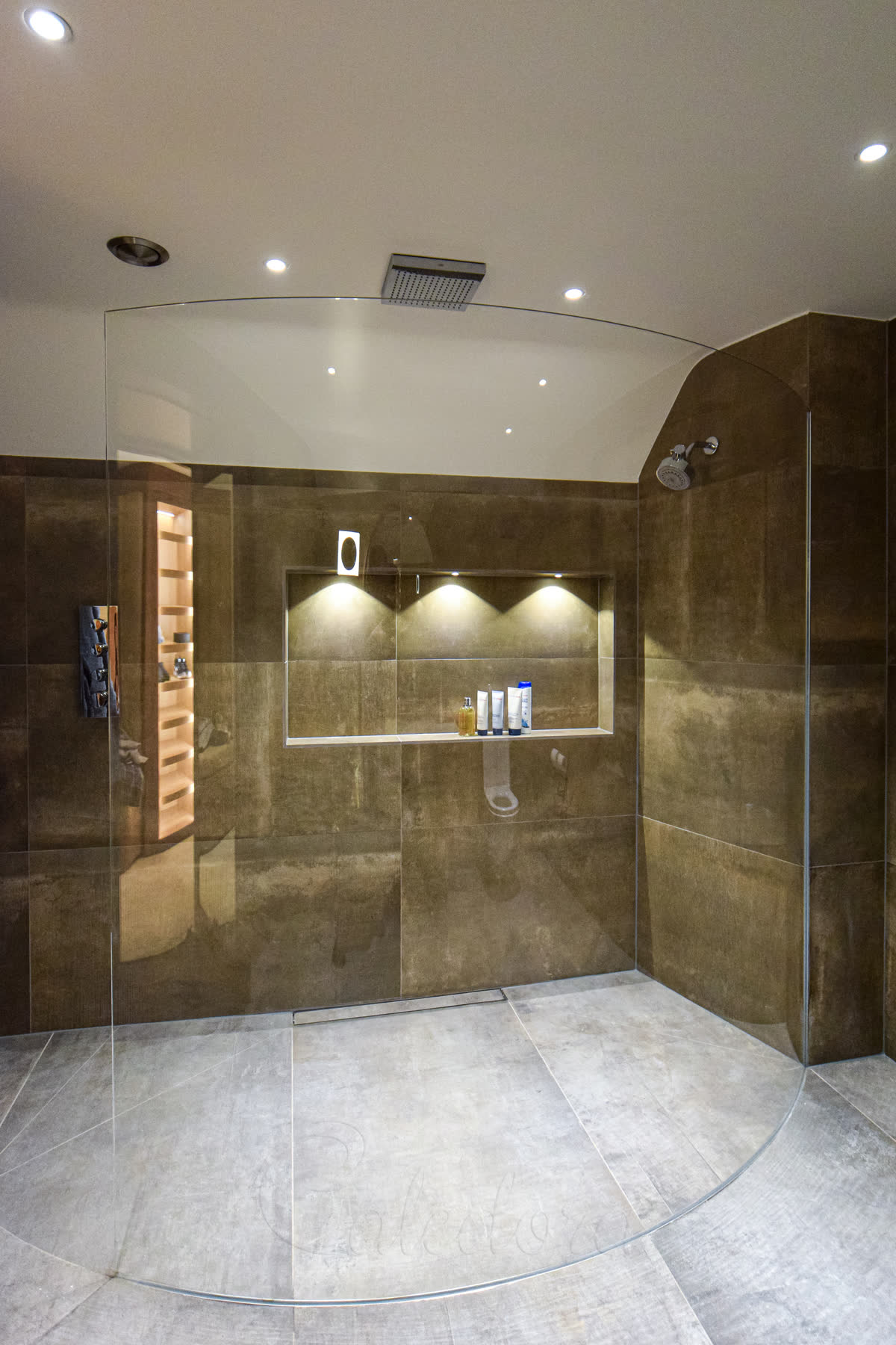 Frameless curved shower screen in a luxury master bathroom with golden stone tiles in Sussex