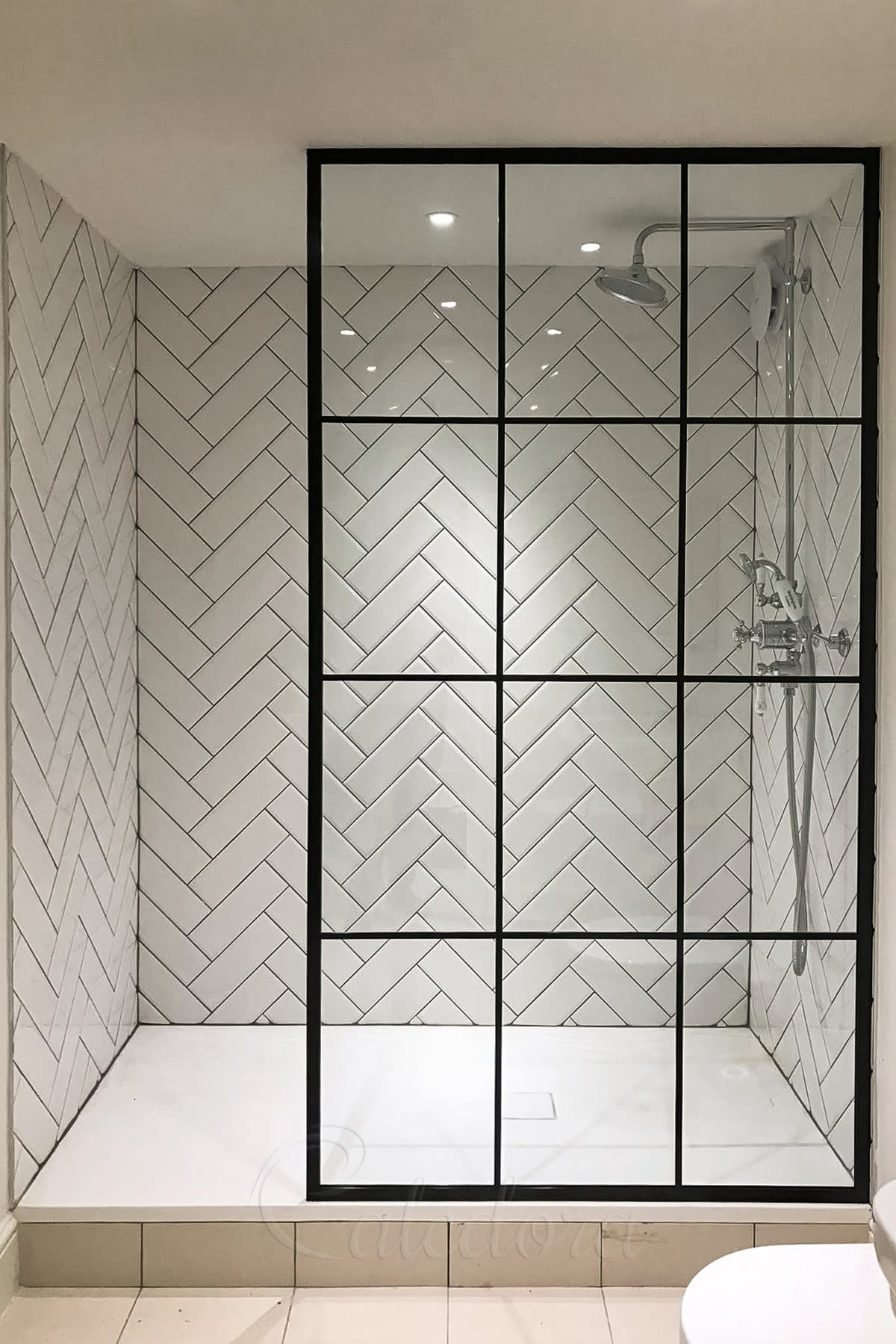 Walk-in shower screen with Crittall style black frame, low iron glass panels, herringbone tile pattern, industrial design in modern bathroom