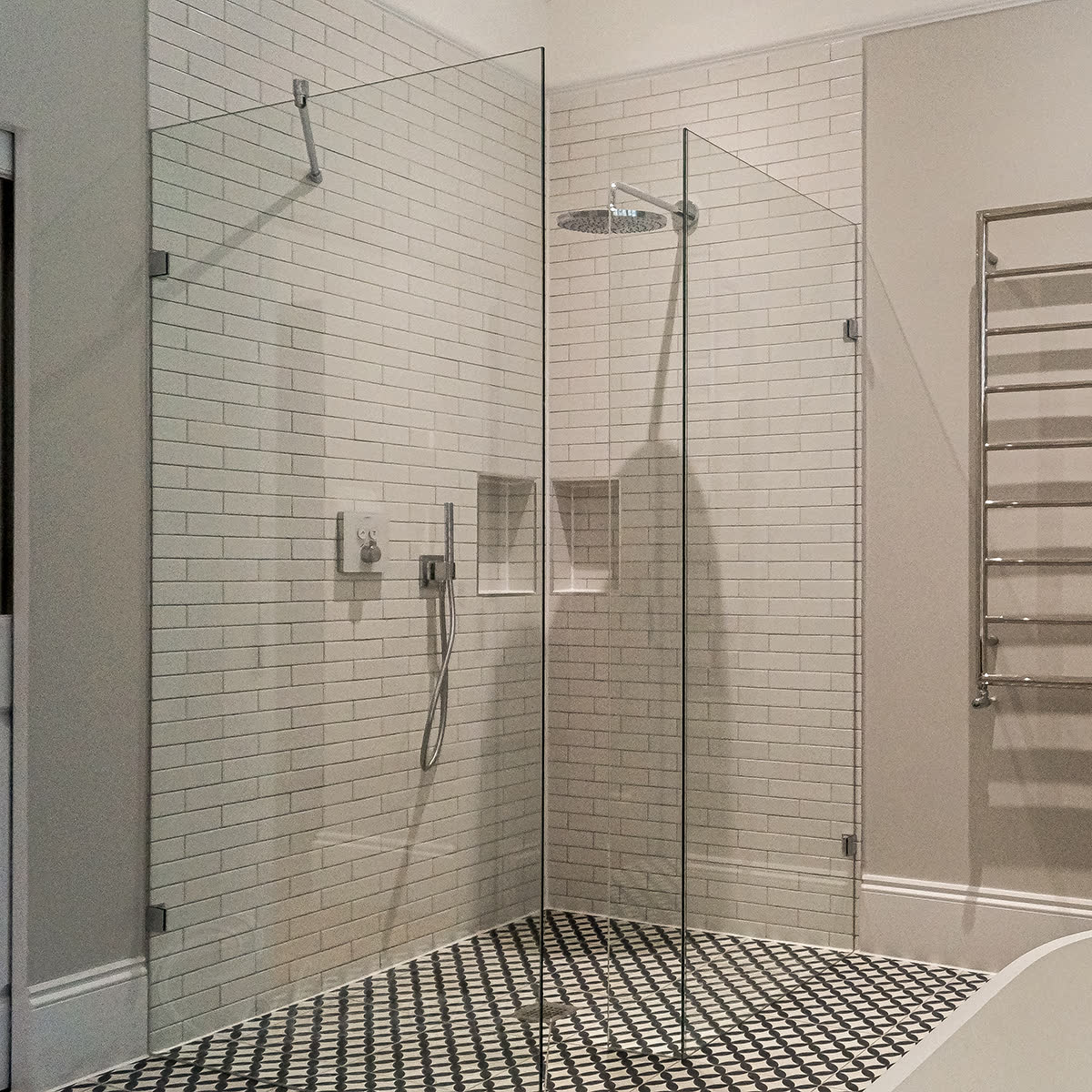 Frameless corner walk-in shower screen attached to the wall with metal wall brackets in a London bathroom