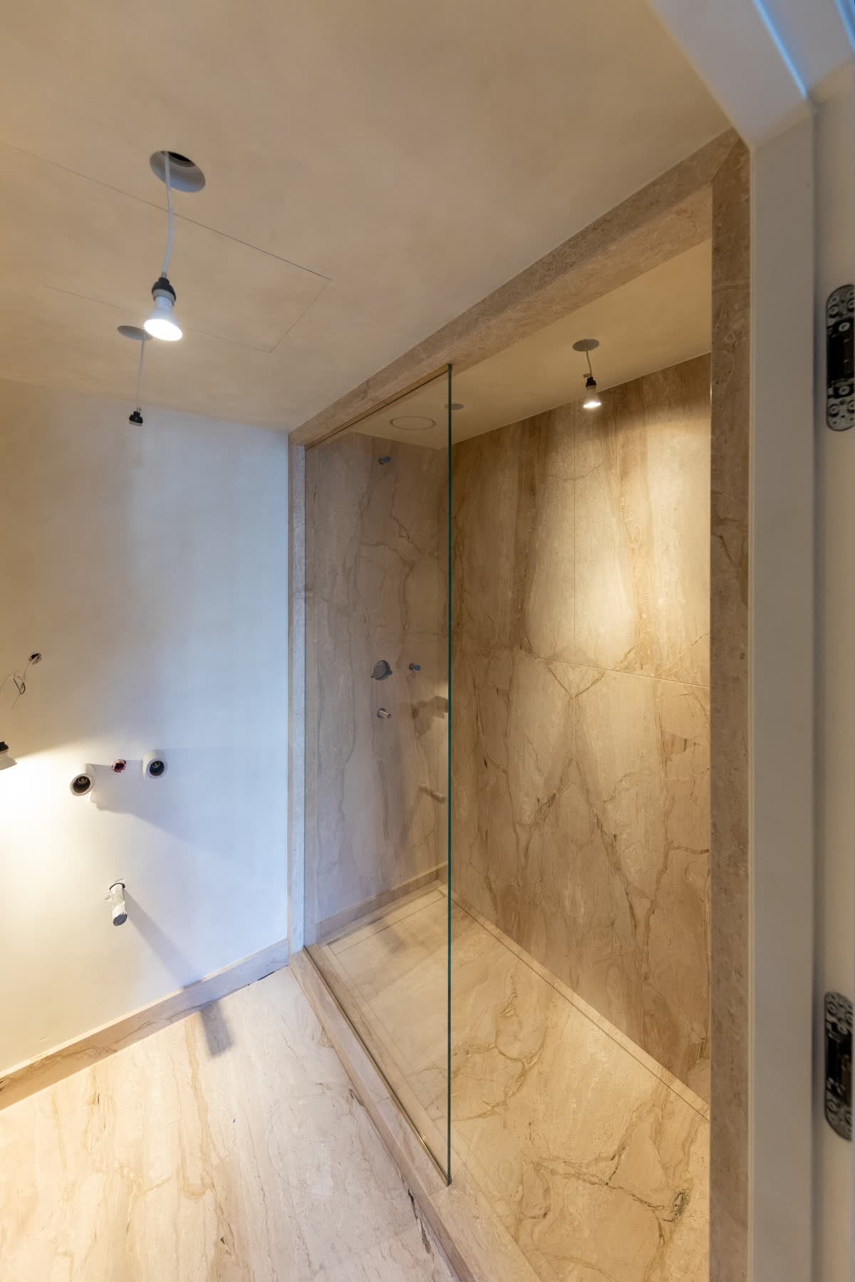 A clear walk-in panel standing on a low stone upstand that runs across the shower opening, the shower floor and the bathroom floor level on either side of it, the opening framed in the same veined stone